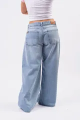 Jeans wide leg de denim rígido en lavado celeste vintage, con diseño de cintura cruzada y cierre asimétrico de doble botón.