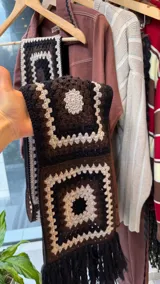 Bufanda con capucha integrada, tejida a mano en crochet con diseño de cuadrados tipo granny square en tonos negro, blanco y marrón.