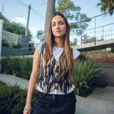 Chaleco corto con estampado abstracto en tonos dorados y azules, escote en V y cierre frontal con botones de madera.