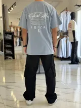 Remera oversize color beige, con mangas corta y gran estampado gráfico en la espalda con texto en negro.