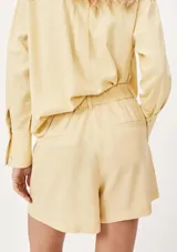 Short de corte recto y tiro alto, confeccionado en tela de lino color amarillo claro. Presenta cintura con elástico en la parte posterior, trabillas para cinturón y bolsillos laterales.
