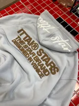 Hoodie de color celeste con capucha y diseño estampado en relieve en la espalda con texto en color marrón. Presenta un corte holgado y cómodo.