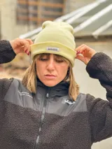 Gorro beanie de lana color amarillo claro, con tejido acanalado y pequeña etiqueta rectangular bordada al frente con la inscripción "Board Brand".