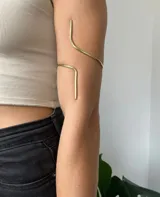 Brazalete de bronce dorado, abierto y ajustable para usar en el brazo o antebrazo.