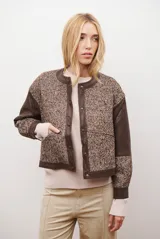 Chaqueta bomber color bordó con mangas de cuero sintético marrón y cuerpo de tweed con patrón de espiga. Cierre frontal con botones a presión y cuello redondo.
