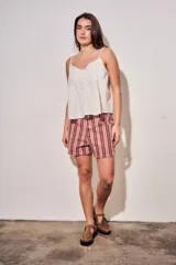 Blusa color off white de algodón peinado, sin mangas, con tirantes finos, escote en V con detalles de encaje y bordados, y pliegues decorativos en los laterales.