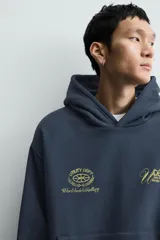 Sudadera tipo hoodie de corte relajado en color azul oscuro con efecto lavado. Presenta capucha, manga larga, bolsillo frontal tipo canguro y detalles estampados en color dorado en el pecho.