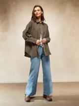 Camisa de pana color oliva, con corte oversize, cuello clásico, cierre frontal con botones metálicos y mangas largas con puños abotonados.