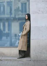 Gabardina larga de piel caprina en color beige, con solapas amplias, cierre cruzado con botones y cinturón ajustable del mismo material.
