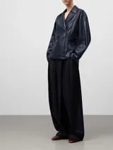 Chaqueta tipo biker de cuero sintético en color azul oscuro, con solapas, cierre frontal cruzado con cremallera, cintura entallada y mangas largas. Cuenta con bolsillos delanteros con cremallera invisible.