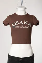 Remera baby tee de morley color chocolate, de calce ajustado al cuerpo y manga corta, con cuello redondo y diseño estampado frontal.