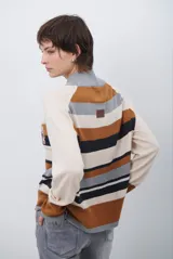 Polera de tejido de punto con diseño de rayas horizontales en tonos beige, marrón, gris y negro. Presenta cuello redondo y mangas largas con puños en contraste.