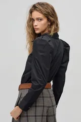 Camisa negra de algodón con cuello clásico, mangas largas con puños y hombros fruncidos que aportan volumen.