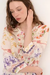 Blusa de manga tres cuartos color beige con estampado floral multicolor, escote en V y detalles de volados frontales junto a la botonadura.