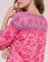 Remera evasé de manga tres cuartos y escote bote, confeccionada en rayón elastizado de color rosado con textura flameada y estampado floral en tonos fucsia y azul.