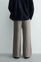 Pantalón relaxed fit color marrón con patrón de espiga, confeccionado en tejido con viscosa. Presenta pliegues frontales, bolsillos laterales y bolsillos traseros de vivo. Cierre frontal con cremallera y botón.