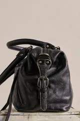 Cartera de cuero verde militar con acabado gastado, cuerpo blando, asas de mano, bolsillos frontales con cierre y tiras colgantes.