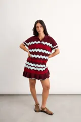 Vestido corto de punto con patrón en zigzag de franjas azules, marrones y amarillas, cuello polo con cierre frontal de un botón, mangas cortas y volado en el ruedo.