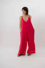 Mono enterito de lino color fucsia, con escote en V, tirantes dobles regulables, bolsillos laterales y detalles de costuras decorativas en contraste en el escote y los tobillos. Presenta una silueta amplia y relajada de pierna ancha.