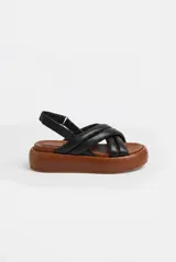 Sandalias de plataforma con capellada de tiras cruzadas acolchadas de cuero color negro, base marrón de goma EVA y tira trasera con ajuste mediante hebilla metálica.