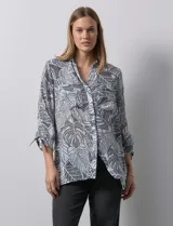 Camisa estampada con hojas en tonos celeste, naranja y verde. Tiene cuello con solapa, abertura central con botones, bolsillos aplicados en la parte delantera y mangas 3/4 con lazo.