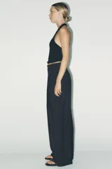 Pantalón de tiro alto color rojo vibrante, de corte ancho y pierna recta, con pliegues marcados en la parte delantera. Presenta cierre frontal con botón y cremallera, y bolsillos delanteros.