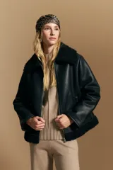 Campera tipo gamulán de cuero sintético negro, con interior y detalles de corderito sintético al tono en cuello y ruedo. Presenta cierre frontal metálico y diseño de silueta relajada.