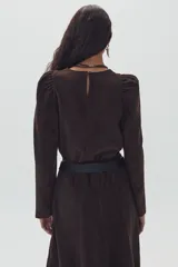 Camisa marrón de gamuza con cuello redondo, mangas largas abullonadas y falda midi acampanada. Incluye cinturón ancho de cuero negro.