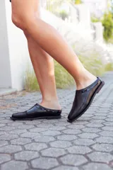 Zapatos tipo mules de cuero negro, con punta fina y detalle de charol en el borde superior.