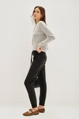 Pantalón tipo babucha de gabardina elastizada, color negro, con cintura elástica ajustable mediante cordón, puños en los tobillos, bolsillos diagonales frontales y bolsillos traseros con solapa y botón.