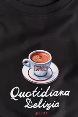 Remera oversized en punto suave de algodón de color negro con diseño estampado en el centro que muestra una taza de espresso y el texto "Quotidiana Delizia ROME". Cuenta con cuello redondo acanalado, hombros caídos y mangas cortas.