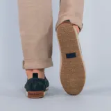 Alpargata de gamuza color verde oscuro, con detalle de elástico lateral a rayas rojas y blancas. Presenta una suela con borde de yute trenzado y base de goma.