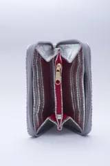 Billetera marrón tipo sobre con cierre de cremallera, confeccionada en cuero con textura tipo cocodrilo y forro textil rojo. Cuenta con múltiples ranuras para tarjetas, documentos y billetes.
