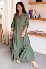 Vestido largo de estilo camisero en color azul, con cuello clásico, cierre frontal de botones y mangas tres cuartos con trabillas. Presenta un diseño de falda con cortes horizontales que le otorgan volumen y movimiento.