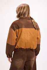 Chaqueta bomber de diseño combinado en tonos tierra, confeccionada con paneles de gamuza y detalles en cuero sintético. Presenta cierre frontal con broches metálicos, bolsillos frontales con tapa y puños elásticos.