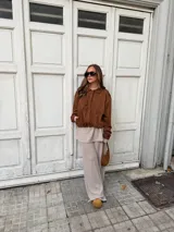 Campera de estilo bomber confeccionada en simil gamuza color marrón, con cuello camisero, cierre frontal oculto y puños elásticos.