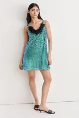 Vestido corto de tirantes, cubierto de lentejuelas reversibles que cambian de color entre azul y verde. Presenta un escote en V adornado con flecos negros.