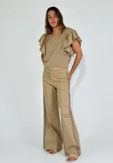 Pantalón de tiro bajo color beige, estilo acampanado, con costuras contrastantes visibles en los laterales y bolsillos frontales con solapa.