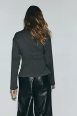 Top de manga larga confeccionado en punto de algodón, con cuello redondo, hombros caídos y detalle de frunces laterales que generan un bajo acampanado.