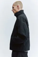 Campera rompevientos de nylon color negro, repelente al agua, con cuello elevado, cierre frontal y bolsillos laterales. Cuenta con forro de malla y puños con elástico.