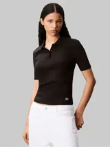 Chomba de Calvin Klein confeccionada en tejido canalé de algodón con elastano. Presenta cuello tipo polo con cartera de dos botones, mangas cortas y un ajuste estructurado. Incluye una pequeña insignia de la marca en el dobladillo inferior.