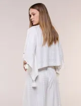 Blusa blanca de silueta holgada con sutil trama en hilo metalizado lurex, escote en V con pechera tejida en crochet y apliques de borlas en el contorno del cuello y las mangas.