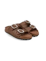 Sandalias planas marrones de cuero entrelazado, con dos tiras ajustables con hebillas grandes decoradas con pedrería brillante y suela de EVA con base dentada negra.