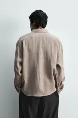 Camisa de corte regular confeccionada en lino, con cuello solapa y cierre frontal de botonadura oculta. Presenta mangas largas con puños abotonados.