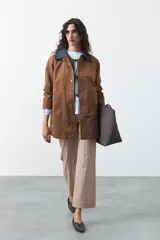 Trench tipo barn jacket color marrón, con cuello camisero en contraste azul marino, cierre frontal con broches y bolsillos amplios. De silueta recta y calce cómodo.