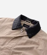 Campera de sarga color beige con corte oversized, cuello de cuero sintético negro con textura trenzada, cierre frontal oculto y bolsillos laterales.