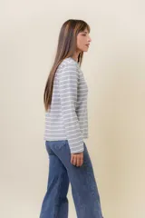 Remera de manga larga con diseño de rayas horizontales verdes sobre fondo crudo, cuello redondo con detalle de volado y cartera frontal con botones.