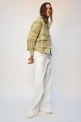 Chaqueta de corte recto confeccionada en tejido con textura de cuadros en tonos amarillos, blancos y negros. Presenta cuello solapa, cierre frontal con botones ocultos, bolsillos de plastrón con solapa en el delantero y mangas largas con puños abotonados.