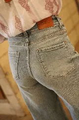 Jean de corte recto y tiro alto, confeccionado en denim de tono azul claro con acabado lavado. Presenta cierre frontal con botón metálico y bolsillos laterales.