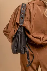 Mochila tipo cartera con tapa, confeccionada en símil cuero color suela. Cuenta con doble compartimento, división interna, cierre de seguridad y bolsillo trasero con cierre. Incluye una correa frontal decorativa con tachas metálicas.